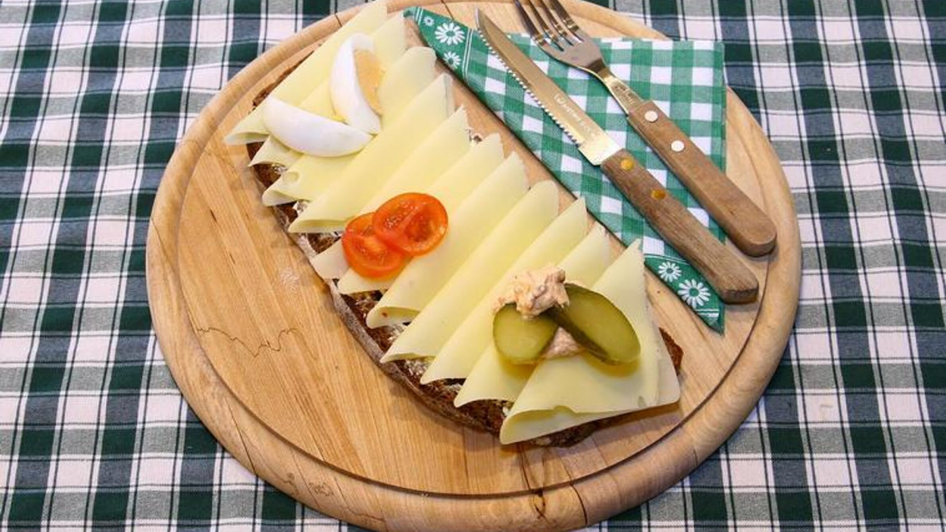 Ein Holzbrett mit einem Käsebrot, garniert mit Gurken, Ei und Tomaten. | © Murheuriger