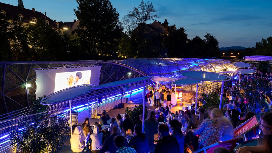 Nachtansicht des Murinsel Cafés mit Besuchern und Lichtspiel. | © Harry Schiffer