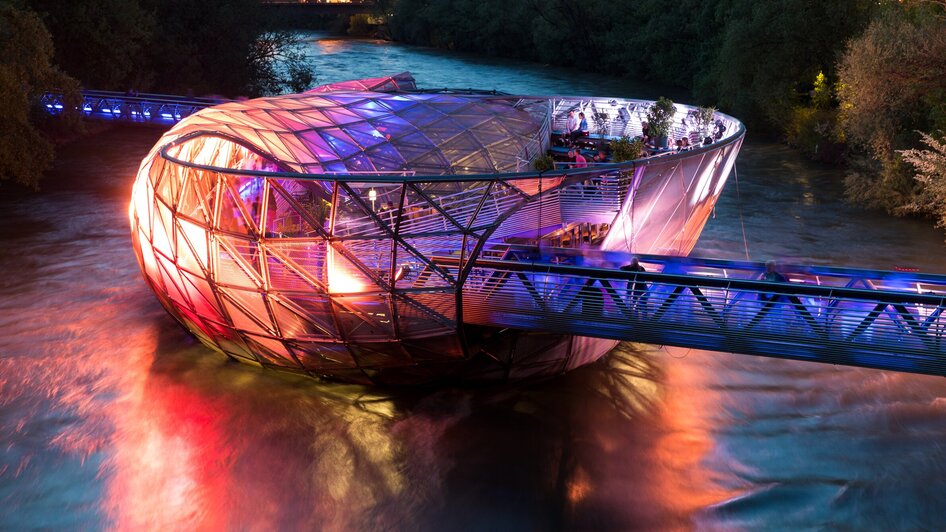 Beleuchtete Murinsel in Graz auf der Mur bei Nacht.