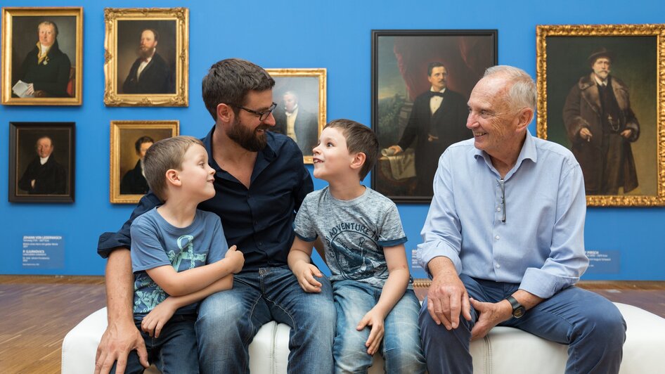 Vater, Großvater und zwei Kinder sitzen zusammen in der Galerie. | © UMJ - Harry Schiffer