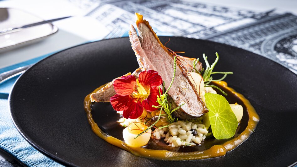 Ein kunstvolles Gericht mit Fleisch, Blüten und Risotto auf einem schwarzen Teller. | © Graz Tourismus - Werner Krug