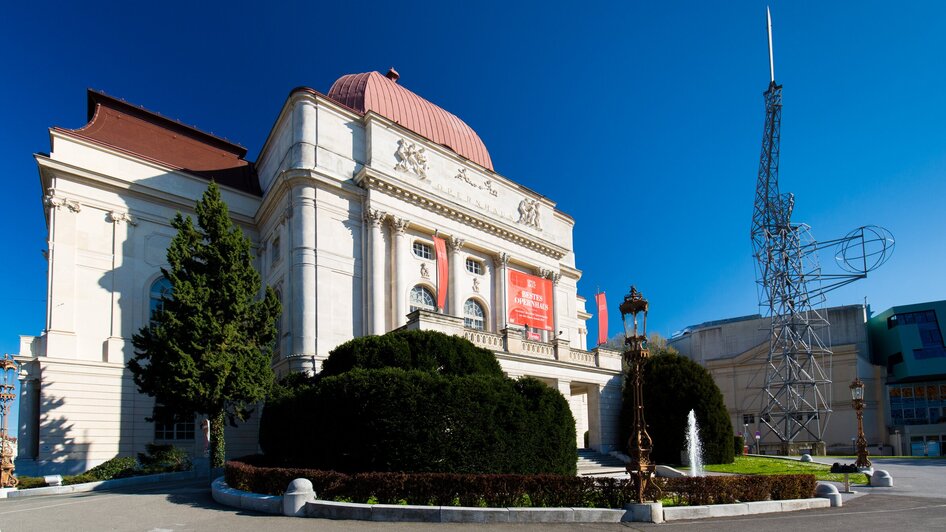 Die Oper Graz unter blauem Himmel mit "Lichtschwert" Statue.