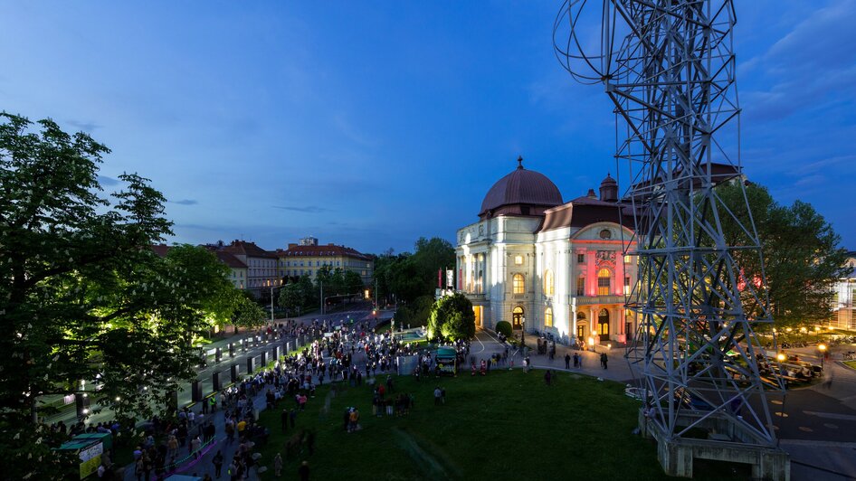 Menschenmenge vor der beleuchteten Oper Graz bei Dämmerung.