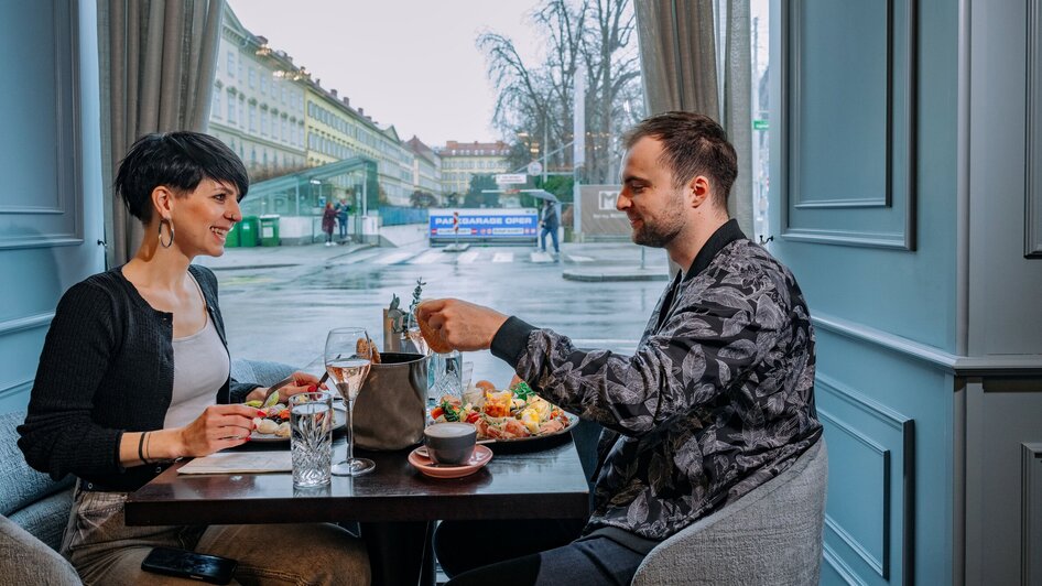 Paar genießt Frühstück im Operncafé in Graz mit Blick auf die Stadt.