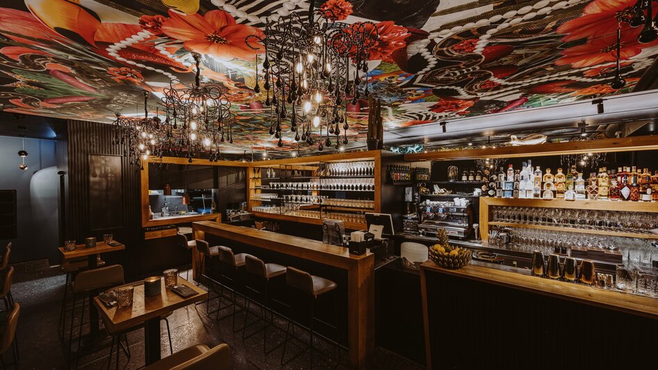 Moderne Bar mit lebhaftem Deckenmuster und eleganten Möbeln. | © Joel Kernasenko