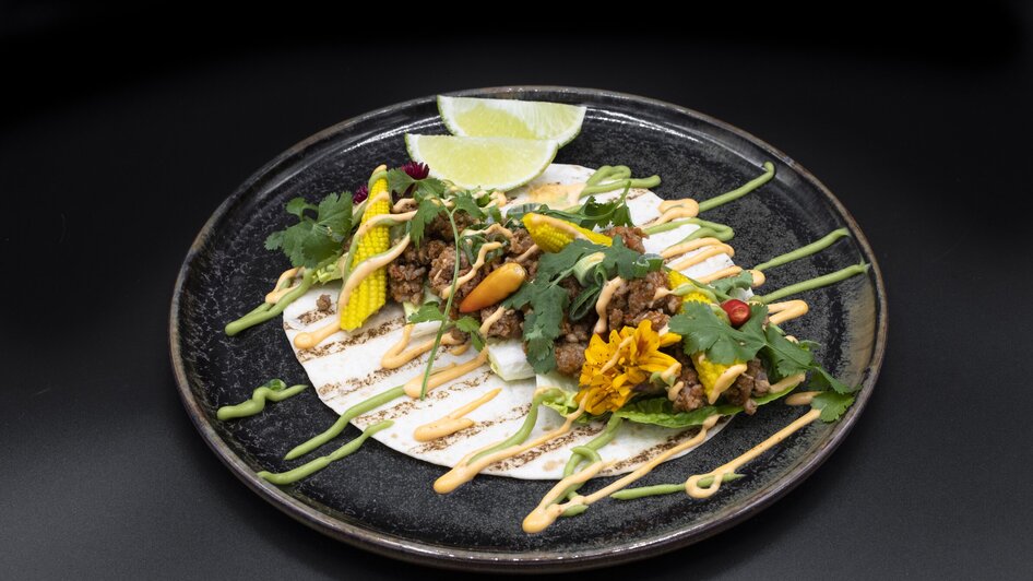 Kreatives Gericht mit Tortillas, Fleisch, frischem Gemüse und Saucen auf einem Teller. | © Jauk Katharina