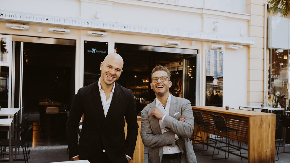 Zwei lächelnde Männer stehen vor einem Restaurant in Graz. | © Joel Kernasenko
