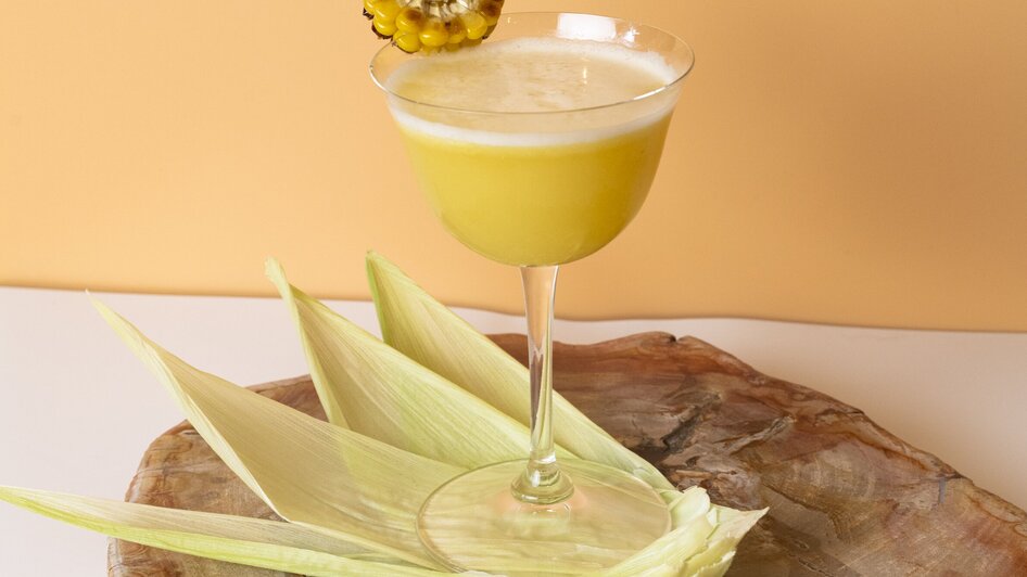 Ein gelber Cocktail in einem eleganten Glas, dekoriert mit einer Scheibe eines Maiskolbens. | © Jauk Katharina
