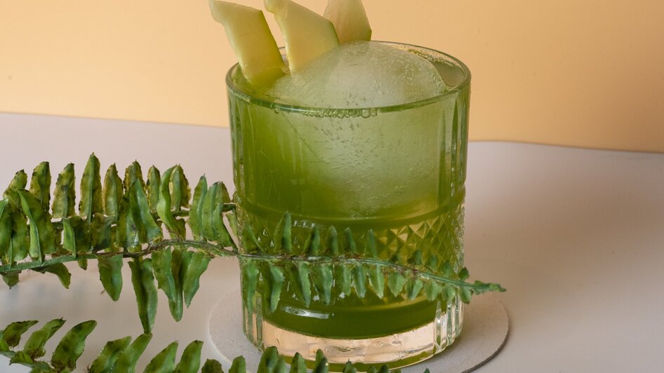 Ein grüner Cocktail mit Apfelstücken, umgeben von Farnen. | © Jauk Katharina