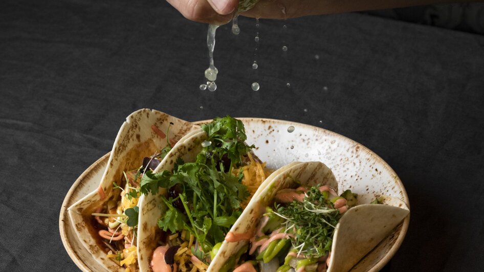 Eine Hand drückt Limette über mehreren Tacos auf einem Teller. | © Jauk Katharina