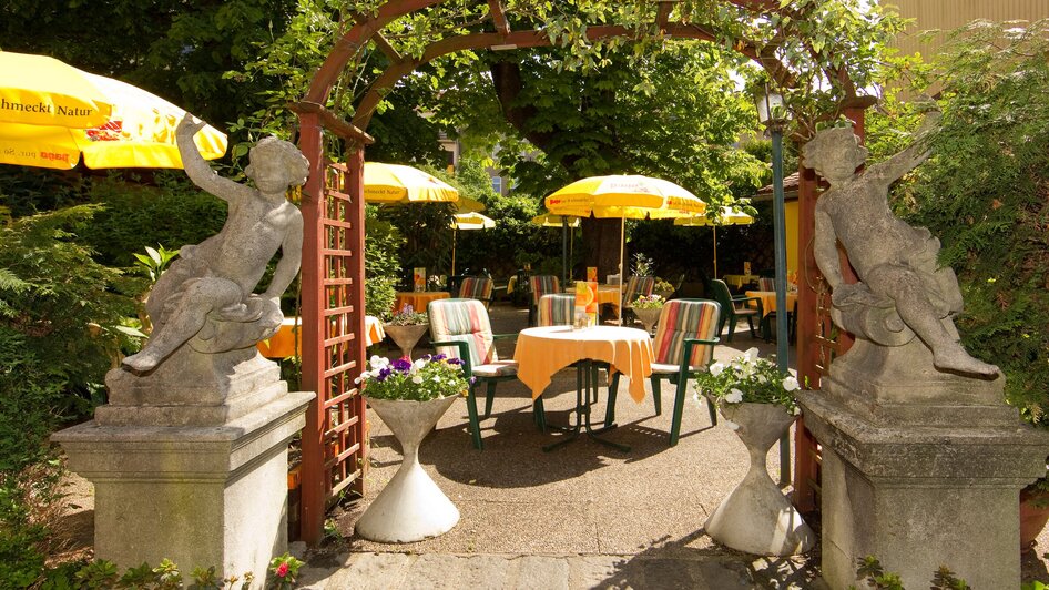 Gemütlicher Garten mit Statuen, Tischen und gelben Schirmen.