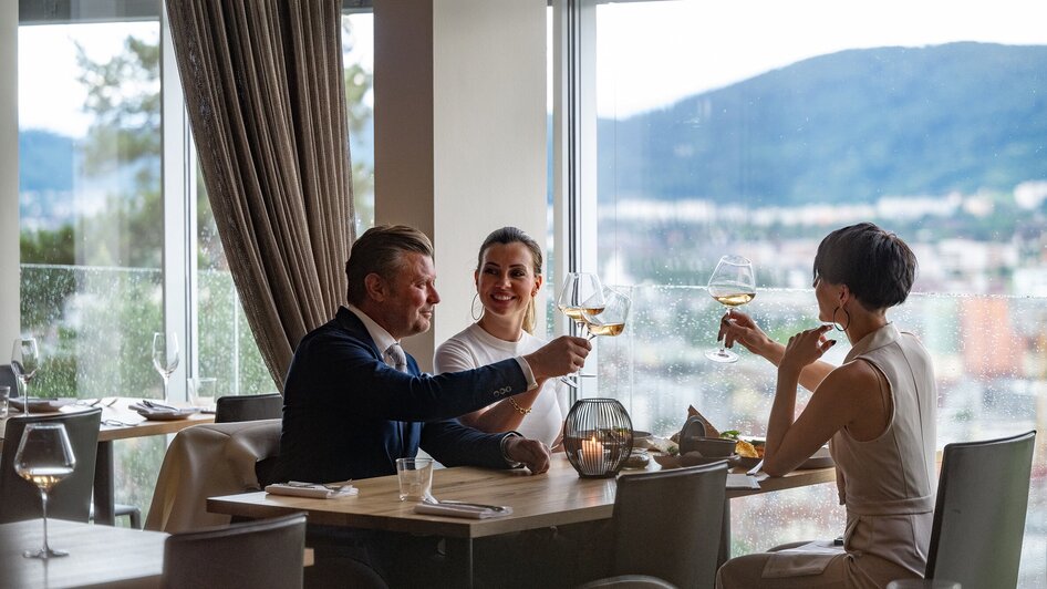 Drei Personen stoßen im Schlossberg Restaurant in Graz an.