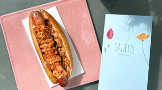 Ein Hotdog auf rosa Platte mit Speisekarte in einem modernen Café. | © Salaettl