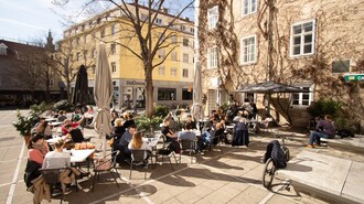 Blick auf das Außencafé Schäffners am Tummelplatz in Graz, viele Gäste sitzen draußen.