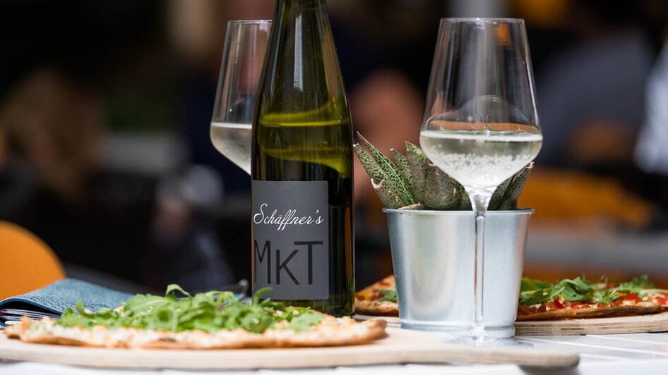 Ein Wein mit Gläsern und Pizza auf einem Tisch in Graz. | © Schäffner