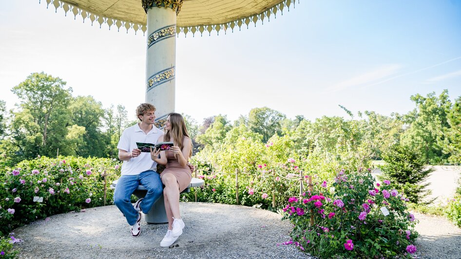 Paar sitzt im Schlosspark von Schloss Eggenberg und schaut in ein Buch.