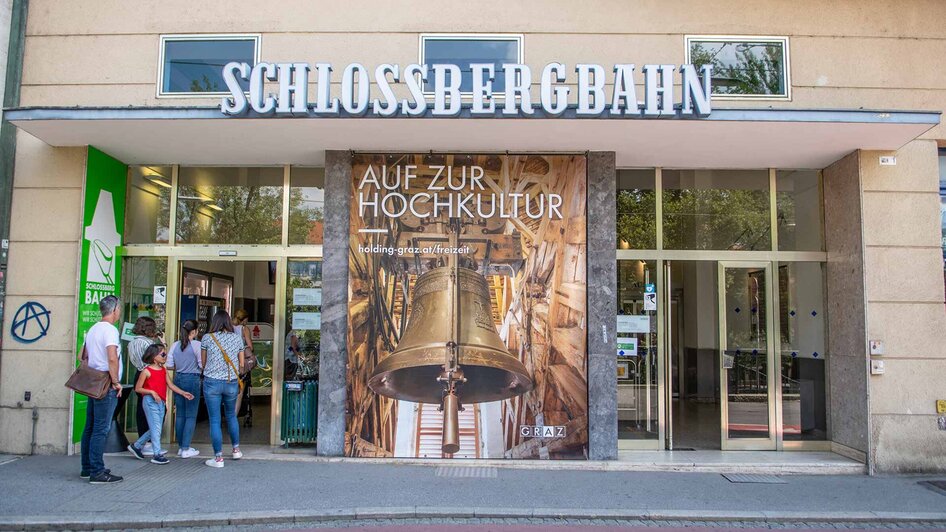 Eingang zur Schlossbergbahn in Graz mit Plakat und Besuchern. | © achtzigzehn - Hinterleitner
