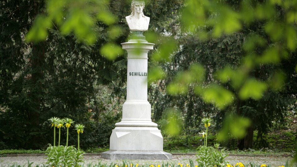 Eine Schiller-Büste inmitten von bunten Blumen im Stadtpark.