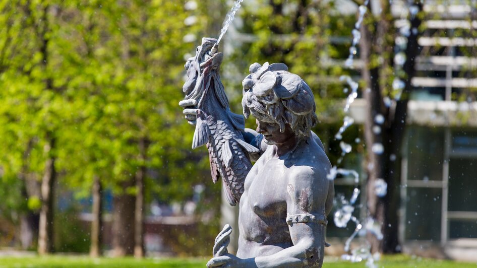 Bronzestatue im Stadtpark Graz mit Wasserfontänen.