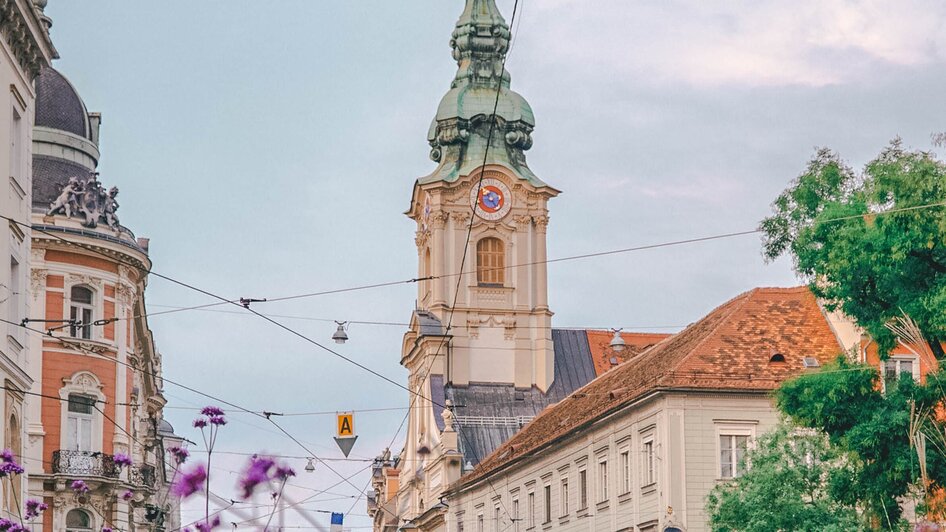 Blick auf die Stadtpfarrkirche in Graz mit Blumen im Vordergrund.