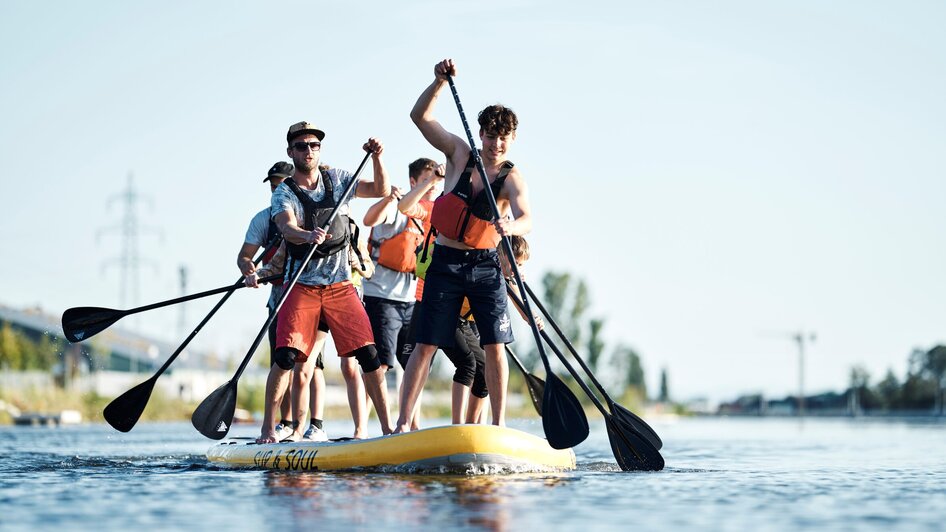 Gruppe von Menschen paddelt auf einem großen SUP im Wasser. | © Stadtstrand Graz - Stefan Leitner