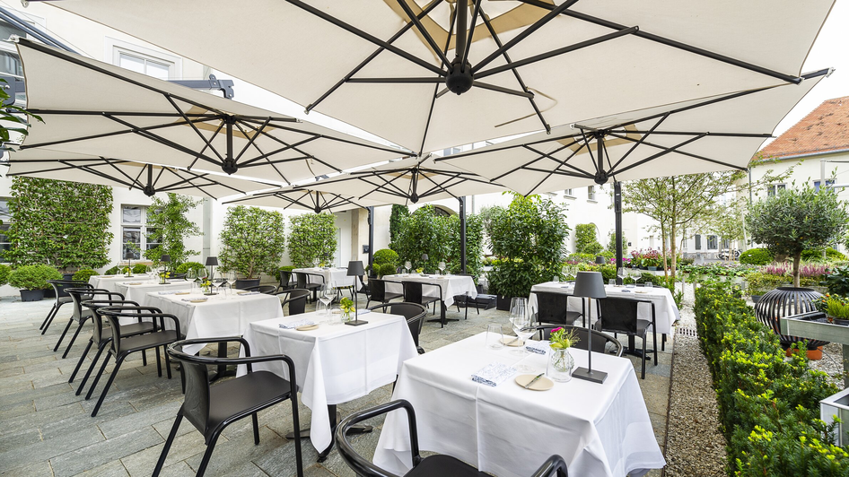 Gemütliche Terrasse mit weißen Tischen und Sonnenschirmen in Graz. | © Paul Stajan