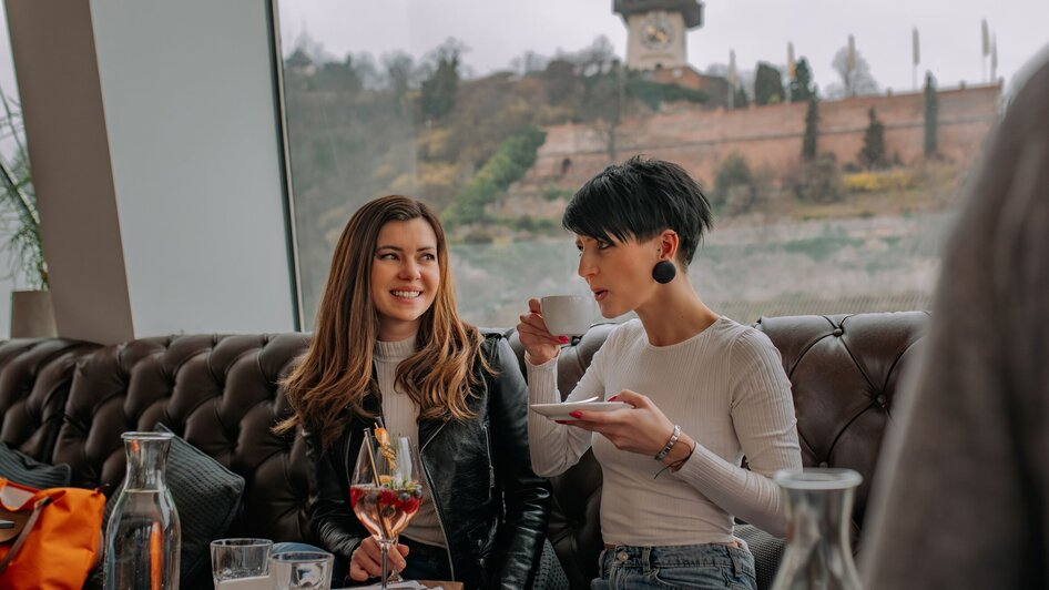 Zwei Frauen im Tagescafé Freiblick in Graz mit Graz Uhrturm im Hintergrund.