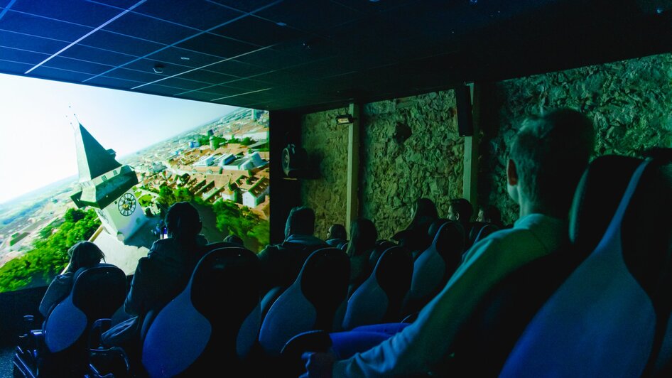 Besucher im 4D Kino im Grazer Schlossberg mit Grazer Uhrturm auf der Kino-Leinwand. | © Region Graz - Mias Photoart