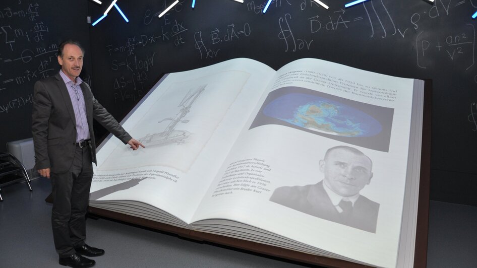 Eine Person zeigt auf ein großes, offenes Buch im Museum.