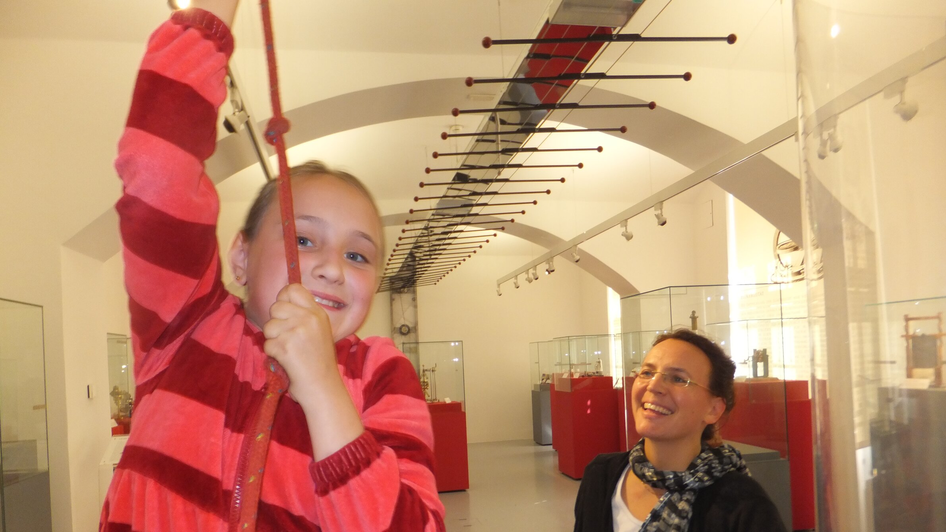 Ein Mädchen spielt in einem Museum, während eine Frau lächelt.