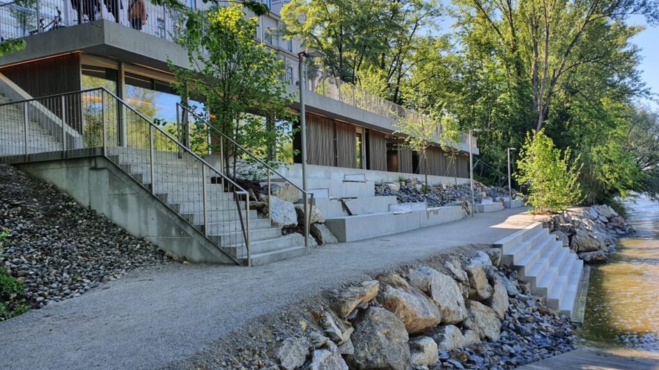 Die gepflasterte Uferpromenade entlang der Mur mit gestuften Treppen und modernen Gebäuden. | © Kajak Club Graz