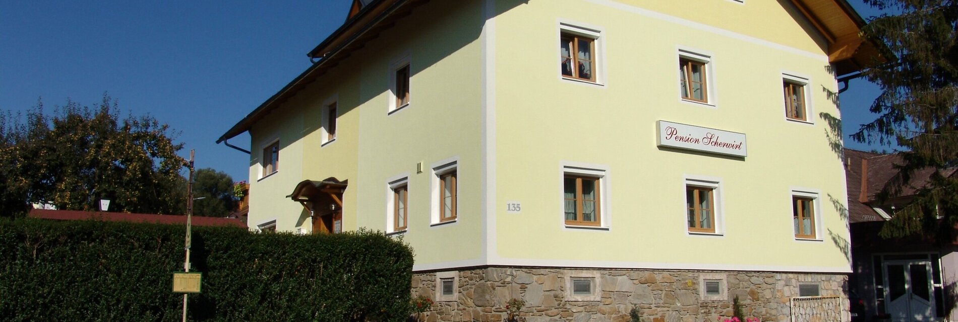 Außenansicht der Pension Scherwirt mit gelber Fassade und Garten.