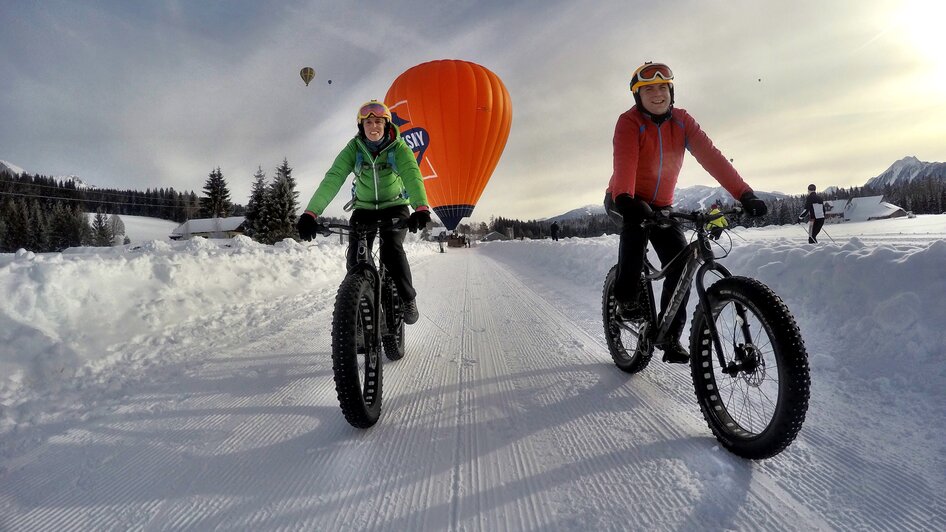 Fatbiker mit Heißluftballon im Hintergrund.