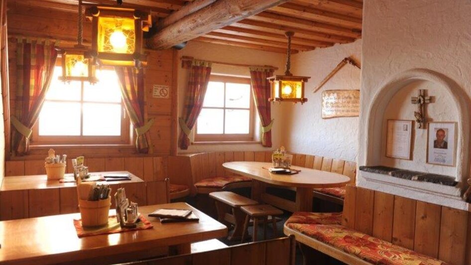 Gemütlicher Gastraum mit Holz-Polsterbänken und Holztischen, warm beleuchtet. | © Weitmoosalm
