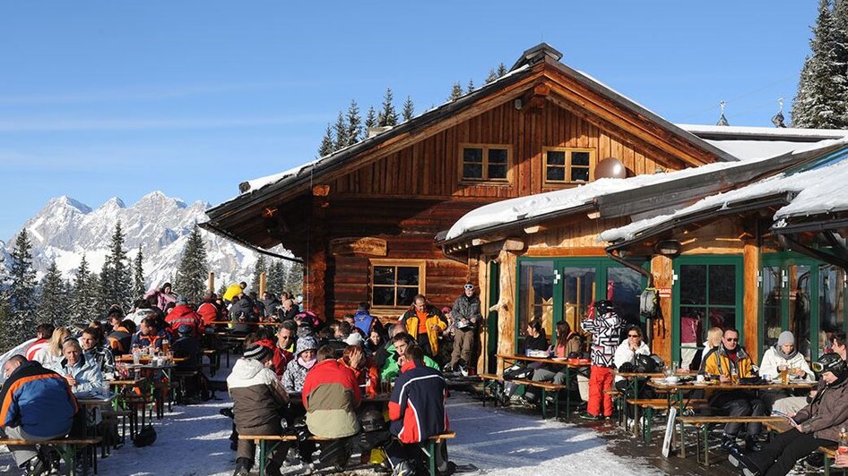 Holzhütte im Schnee mit Terrasse voll mit Menschen | © Weitmoosalm