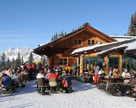 Holzhütte im Schnee mit Terrasse voll mit Menschen | © Weitmoosalm